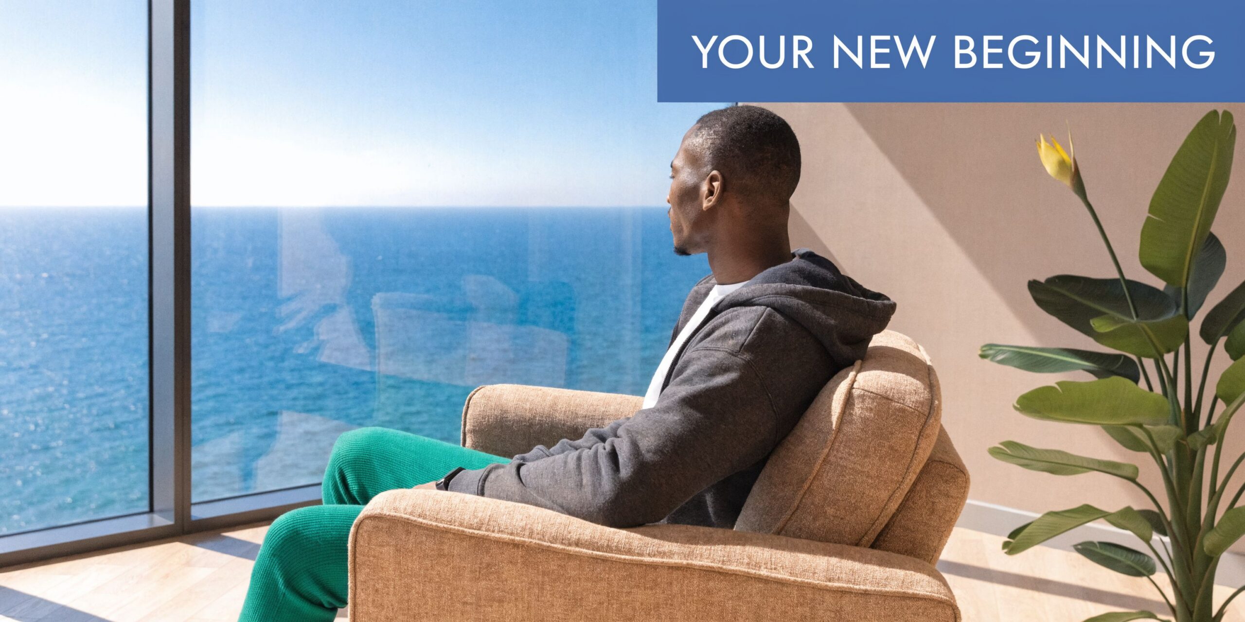 A man sits in a comfortable chair looking out at a calm blue ocean, representing peaceful recovery.