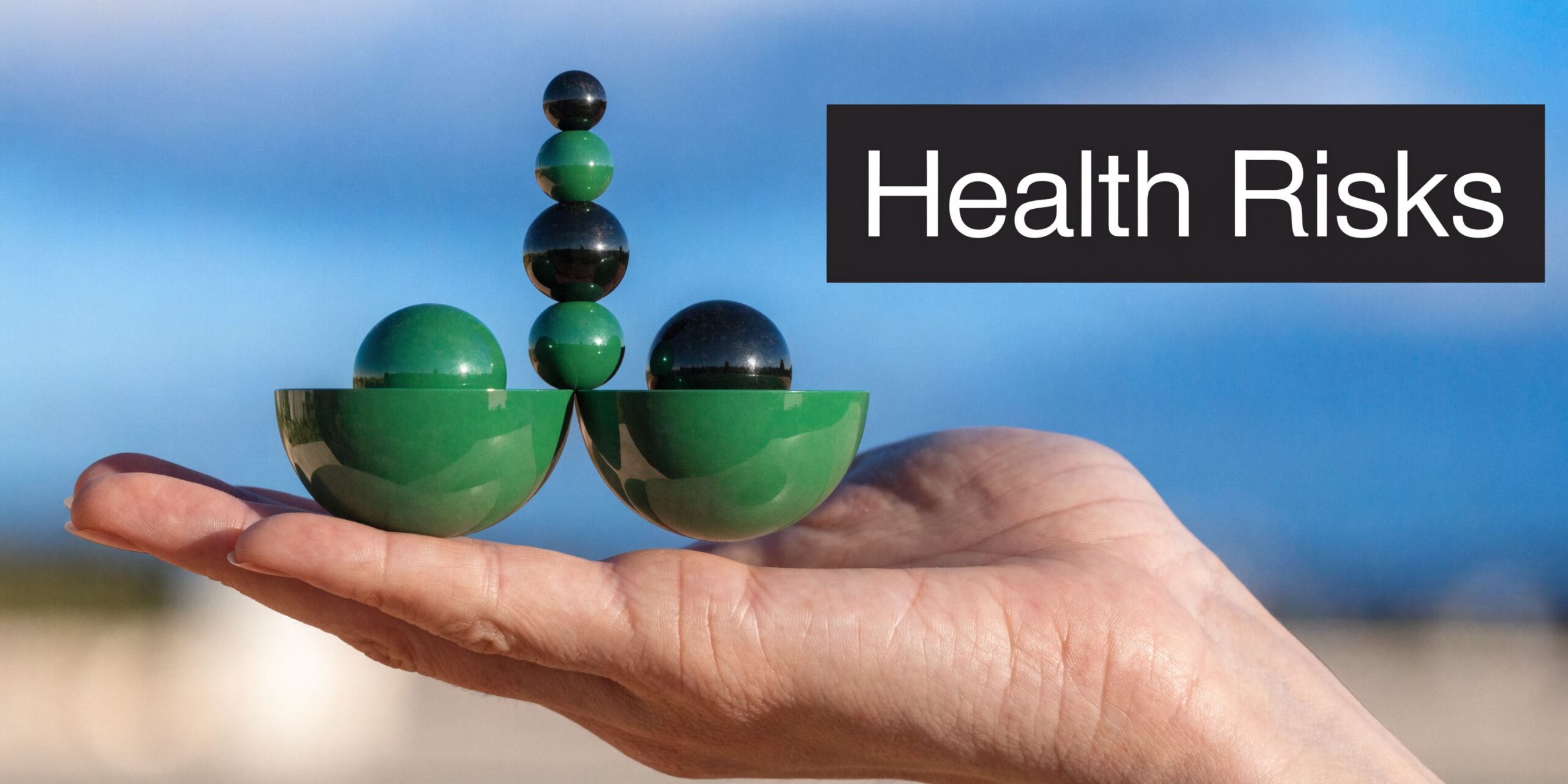 A human hand holding a balanced structure of green and black spheres symbolizing health risk assessment concepts.