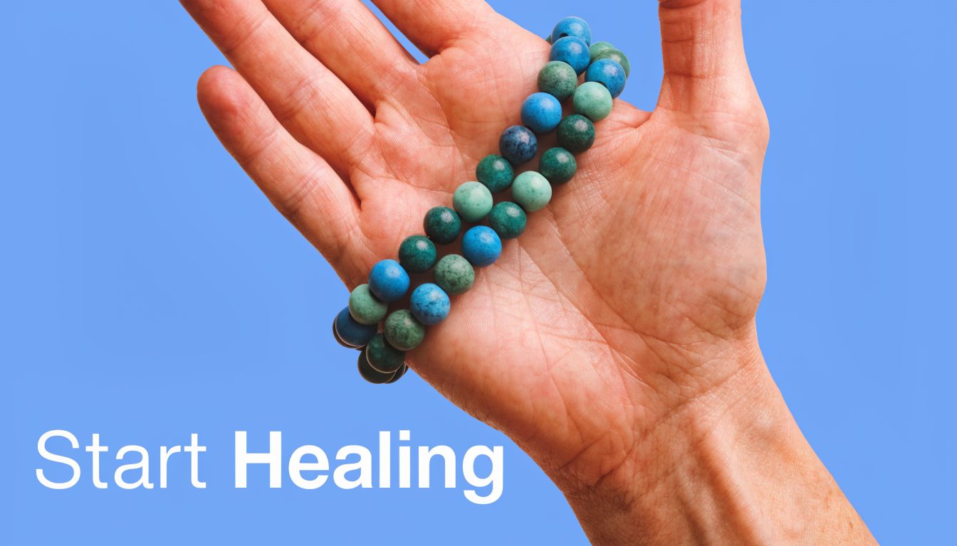 A person holding a blue and green gemstone bead bracelet in their open hand against blue background.