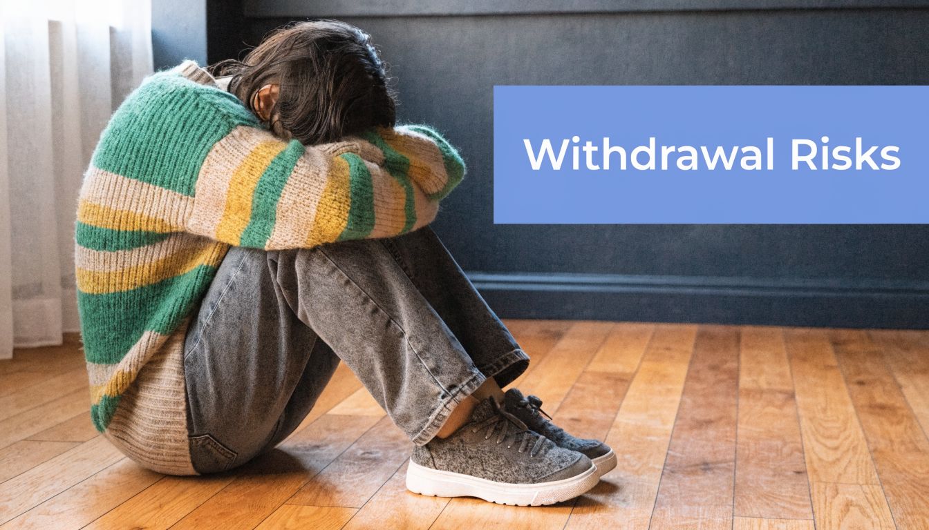A person sitting on a wooden floor, head resting on knees, representing emotional distress and withdrawal risks.