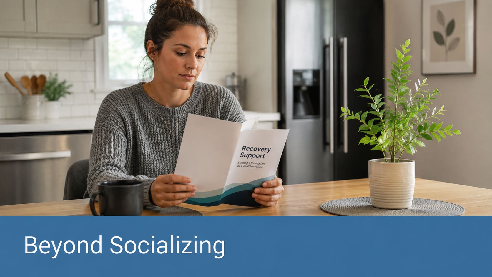A woman reads a recovery support brochure while sitting at a kitchen table with a plant.